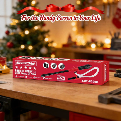 Red box of Battery Operated Liquid Transfer Pump on a wooden table, with holiday decorations in the background