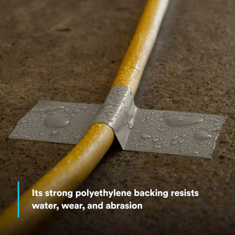 Water droplets on Extra Heavy Duty Olive Duct Tape 6969 sealing a yellow cable on concrete, highlighting water resistance and strength.