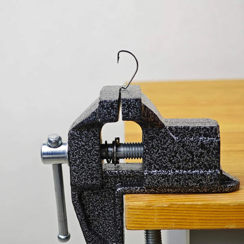 Side view of 2 In 1 Mini Bench Vise And Hook Sharpener For Diyers, clamped to wooden table edge, showing metal jaws and screw mechanism.