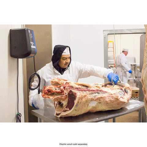 Butcher in white coat and gloves cuts a large beef carcass on a stainless steel table in a meat processing facility.