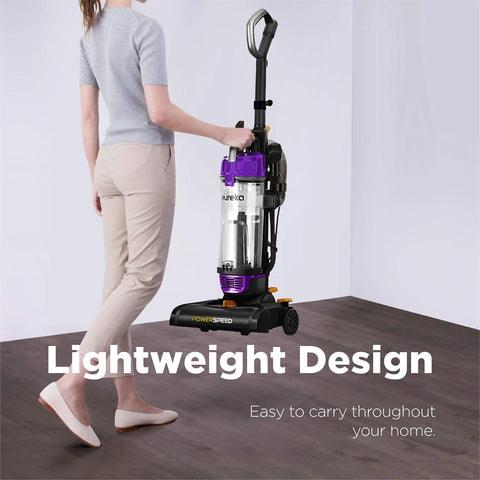 Eureka NEU182B PowerSpeed bagless upright vacuum cleaner, purple with clear canister, carried by a person.