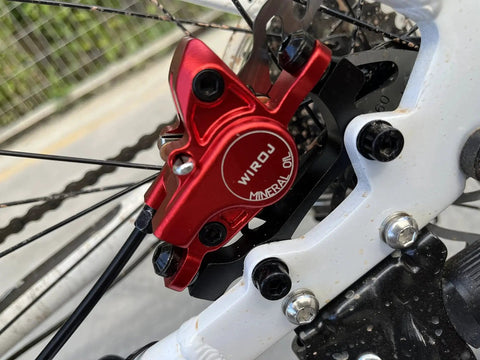 Red WIROJ hydraulic disc brake caliper installed on left-front MTB fork with rotor visible.