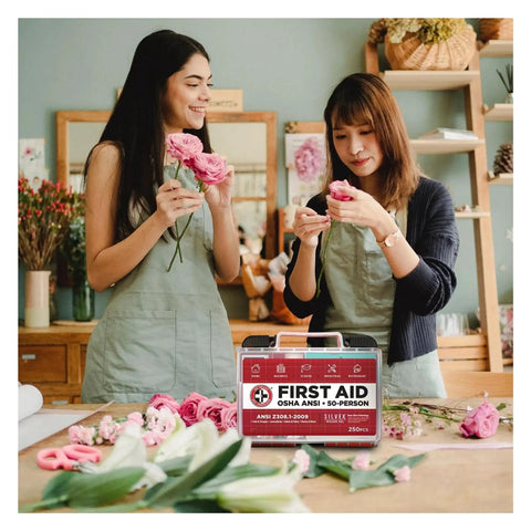 Two people arranging flowers with OSHA And ANSI Compliant First Aid Kit For 50 People, 250 Pieces in the foreground.
