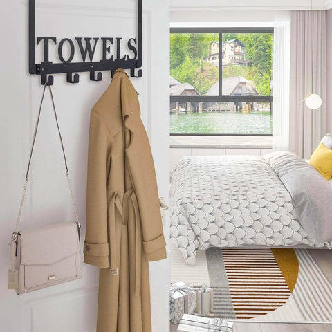 Over-the-door towel rack in black metal with multiple hooks mounted on a white door, holding a beige coat and purse.