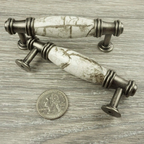 Decorative cabinet pulls with marble design and silver finish next to a quarter for size perspective