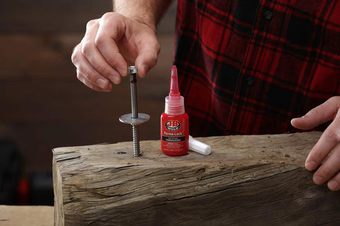 Applying Red High-Strength Thread Locker That Locks Tight And Seals Like A Boss to fastener on wooden surface, 50ml bottle visible