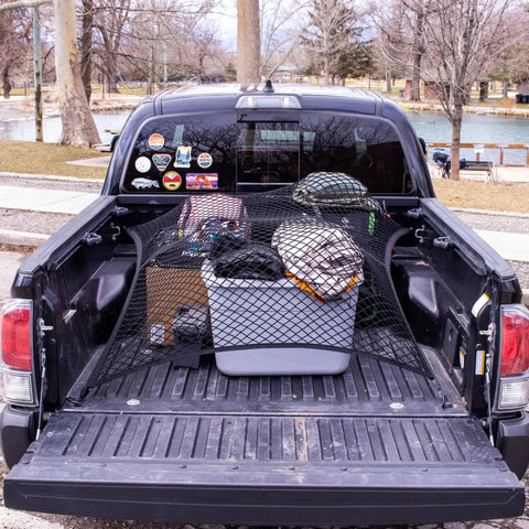 Elastic Cargo Net For Truck Bed And SUV Keeps Lightweight Loads In Place Without Tying Simple Mesh Organizer Fits All Trucks Vans ATVs UTVs SUVs From 4x4 To 7x7 Feet Black securing cargo in a truck bed with various items organized.