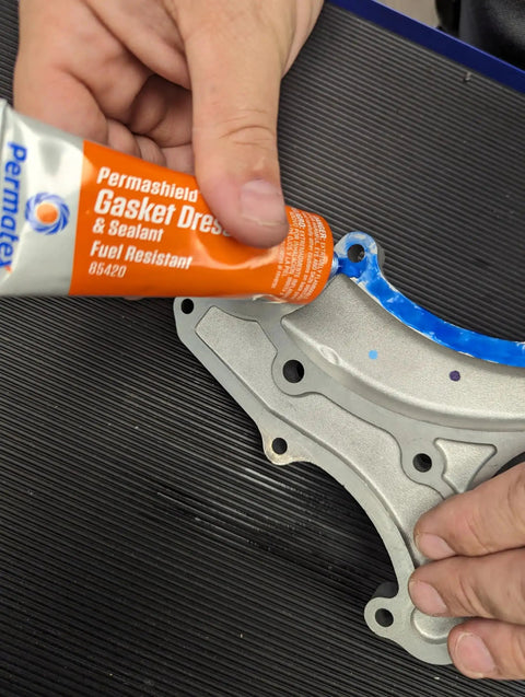 Fuel-Resistant Gasket Dressing And Sealant, Orange, 2 Oz Tube applied to metal joint, shows flexibility and tight seal capability.