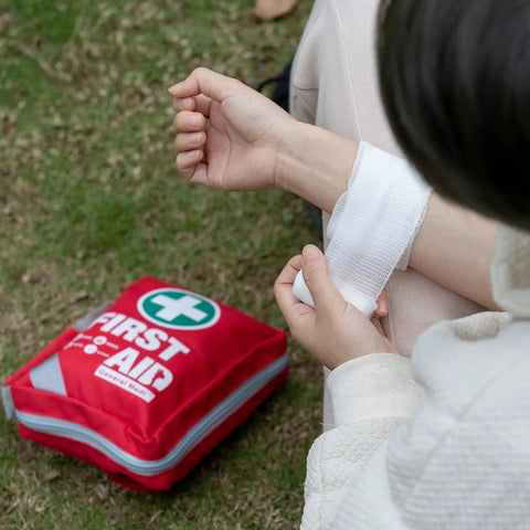 Person applying bandage near Compact 175 Piece First Aid Kit With Reflective Bag Design For Travel Home Office And Vehicle Use