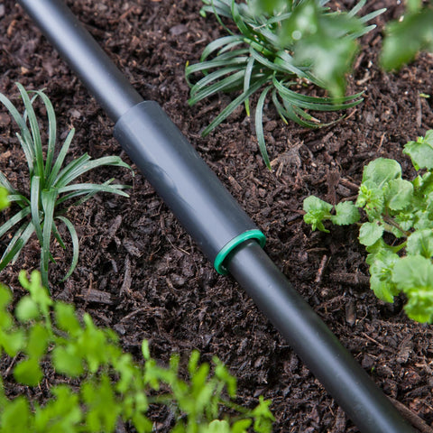 Raindrip 1/2-inch compression coupling on black drip irrigation tubing with a green ring in garden soil