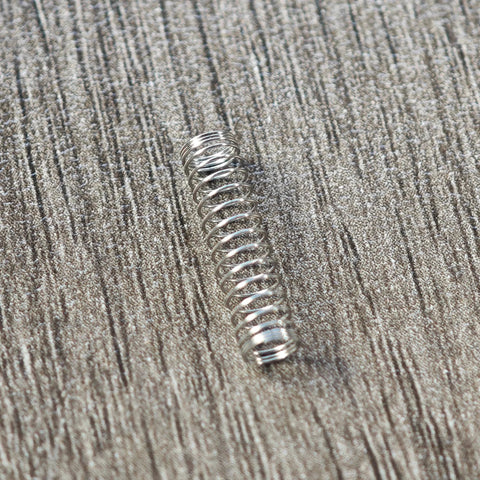 Single stainless steel Cherry MX switch spring on a textured surface.