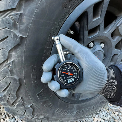 JACO Deluxe Tire Pressure Gauge 100 PSI held at tire valve by gloved hand; black dial gauge.