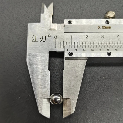 Front view of a silver vernier caliper measuring a small steel ball on a dark surface.