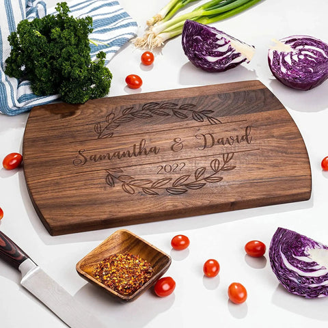 Engraved walnut cutting board with 'Samantha & David 2022', surrounded by vegetables on kitchen counter. Ideal for personalized gifts.