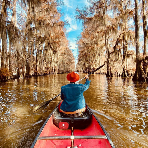 Person paddling a red canoe through a tree-lined waterway, with a Mini First Aid Kit 120 Piece Waterproof Hard Shell Medical Kit visible onboard.