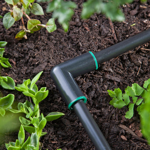 Amazon Raindrip 1/2-in compression elbow, black plastic with green rings, installed in garden irrigation line.
