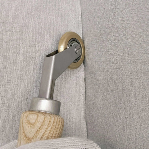 Welding handheld roller with wooden handle and metal arm, brass wheel pressed against light gray fabric.