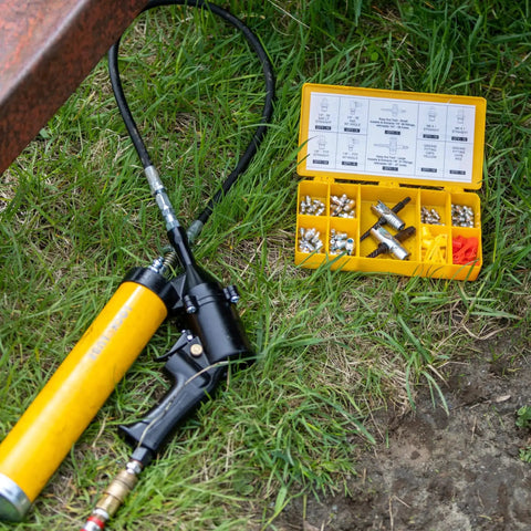 Complete Grease Fitting Replacement Kit With SAE And Metric Zerks For Straight And Ninety Degree Fittings Ten Each Of One Eighth NPT One Quarter Twenty Eight SAE LT Six By One Metric Eight By One Metric Includes Two Multi Tools And Twenty Caps LockNLube on grass with tools