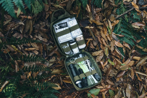 Open green Survival First Aid Kit With Molle Pouch Emergency Medical Gear for vehicles, camping, hiking, and hunting on forest ground.