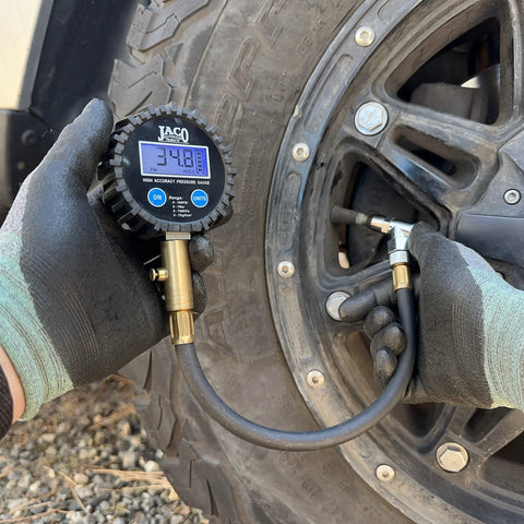 JACO ElitePro digital tire pressure gauge with brass connector and blue display attached to a vehicle tire valve