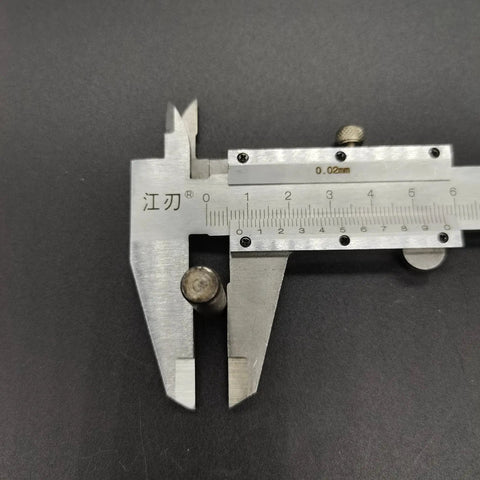 Front view of a steel vernier caliper measuring a small cylindrical metal pin.