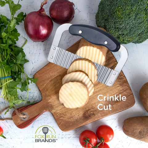 Crinkle Cutter For Veggies And Fruits, Wavy Slicer For Waffle Fries, Chips, Pickles, And More, Durable Stainless Steel Kitchen Gadget By Fox Run on a cutting board with sliced potatoes and vegetables.