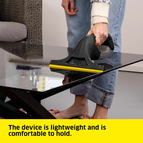 Kärcher WV 1 electric window vacuum squeegee, black with yellow blade, held by a person cleaning a glass table.