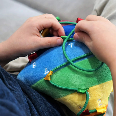 Child interacting with a Colorful Buckle Pillow Sensory Toy For Fine Motor Development And Kid Friendly Hands On OT Therapy With Threading Counting Latches And Zipper Skill Practice SENSORY4U Plushie.