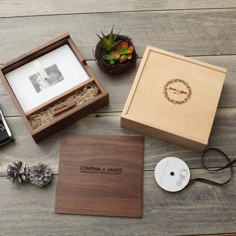 Wooden photo box with names engraved, surrounded by decorative items on a wooden surface.