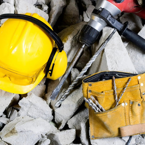 Long 1 Inch SDS Plus Drill Bit for Rotary Hammers, 39 Inch Overall Length, 10mm SDS Plus Shank, 4-Cutter Carbide Tip in pile of concrete, next to yellow hard hat and tool belt.