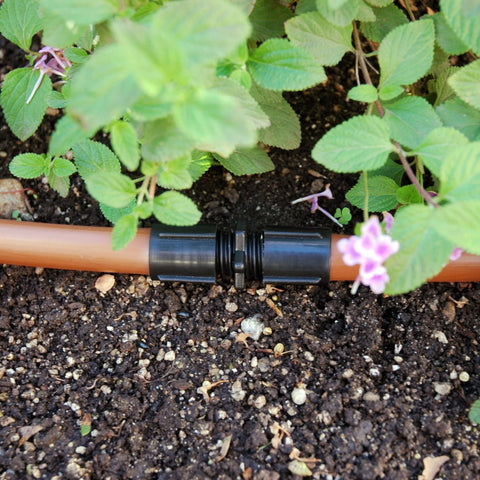 Raindrip S5600UB universal drip irrigation coupling on orange supply tubing, black plastic connector for 1/2, 5/8, and 0.710 in tubing