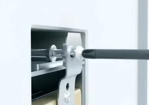 Close-up of an Adjustable Outlet Spacer 50pk being installed with a screwdriver, showing its metal and plastic components.