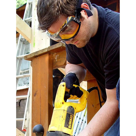 Man wearing clear anti-fog safety goggles with ventilation channel and adjustable elastic strap using power tool on construction site.