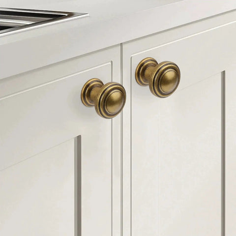 Antique Brass Cabinet Knobs 10 Pack for kitchen cabinets, installed on white cabinet doors, showing its classic finish and durable construction.