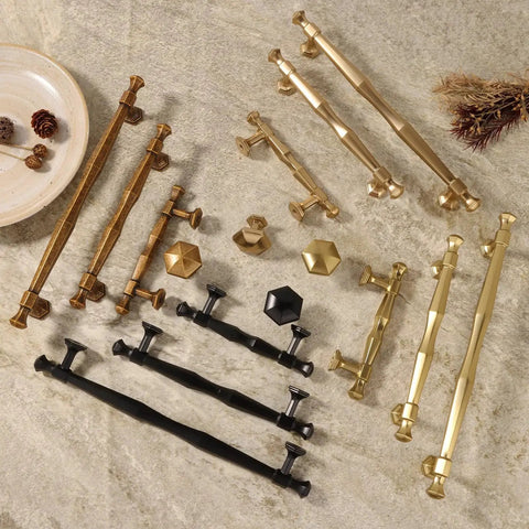 Variety of zinc alloy cabinet pulls in antique brass, black, and gold finishes on stone surface, featuring different designs and sizes.