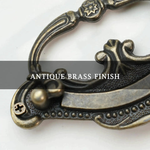 Close-up of antique brass finish on Baroque style drop bail drawer pull for classic furniture restoration.