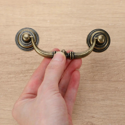 Hand holding vintage bronze drawer pull, part of a Set Of 10 Antique Drop Bail Pulls With 3.5 Inch Center Hole, 4.5 Inch total length