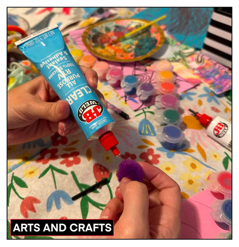 Person using a blue adhesive tube for arts and crafts with colorful materials and supplies around.