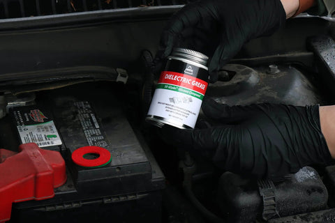 AGS Automotive Solutions Brush Top Can Dielectric Silicone Grease Compound for All Electrical Components and Connectors, 4oz being held near car battery