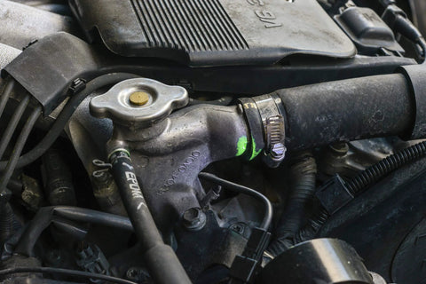 Automotive engine bay showing radiator cap, metal thermostat housing, coolant hose, and hose clamp