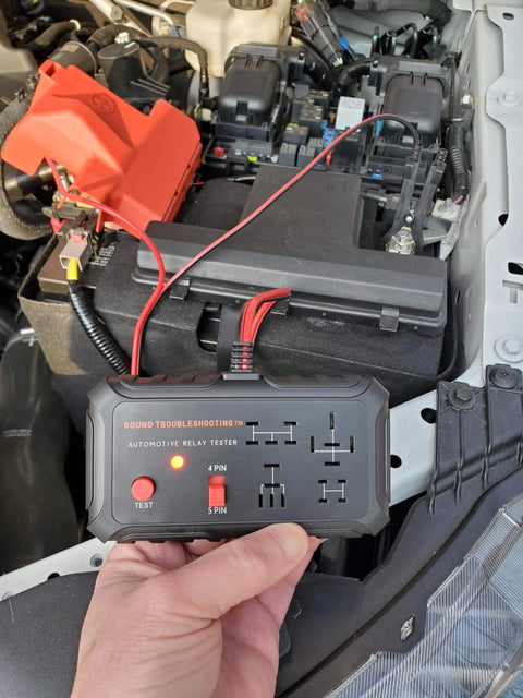 Automotive Relay Tester With Puller For 12V Cars And Trucks, held above car engine, shows LED status alerts and pin detection