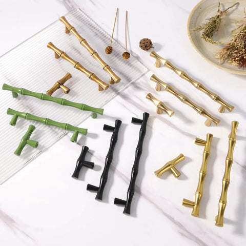 Various styles of bamboo-inspired cabinet pulls in gold, green, and black, arranged on a marble surface with decorative elements.
