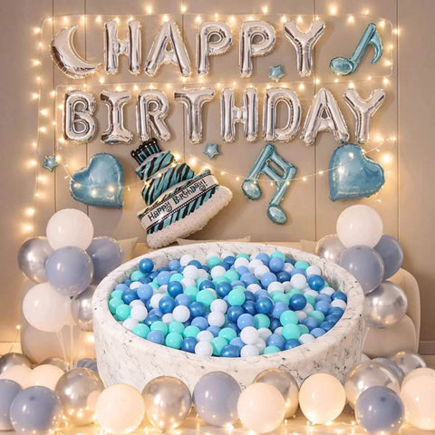 Birthday party setup with ball pit filled with blue, white, and green balls; "Happy Birthday" balloons and decorations surround the scene.