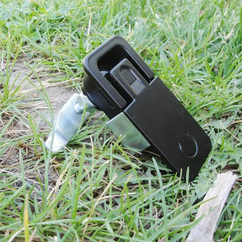 Two piece compression latch with flush sealed lever, lift and turn adjustable grip in black, placed on grass.