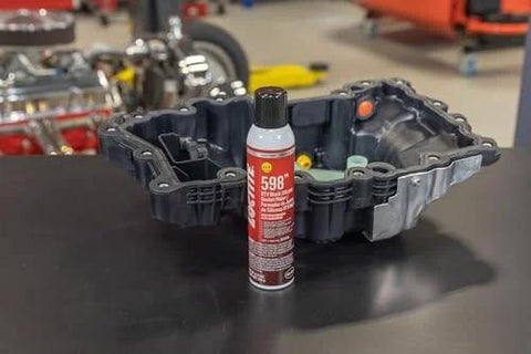 598 Black High Temp RTV Silicone Sealant For Auto Use OEM Approved Performance Engine Building And Repair Grade Heat Resistant Adhesive Sealant Durable Gasket Maker For Intake Exhaust And Engine Surfaces next to engine part on workbench.