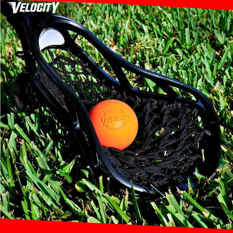 Black lacrosse stick head with orange ball on grass