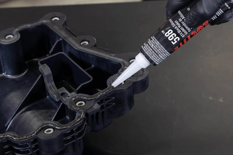 Automotive RTV Silicone Gasket Maker Black 598 being applied to engine seal surface, 80 milliliters pack shown in use