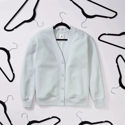 Maximize closet space with a 50-pack of slim velvet non-slip hangers holding a white sweater on a wall display.