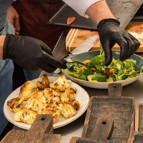 Chef wearing Black Vinyl Medical Exam Gloves Disposable Latex Free Powder Free 100 Count preparing salad and grilled vegetables.
