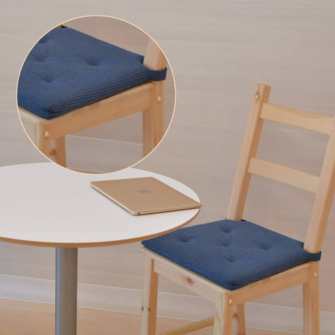 Wooden chair with blue cushion next to round white table with laptop, focus on cushion detail.